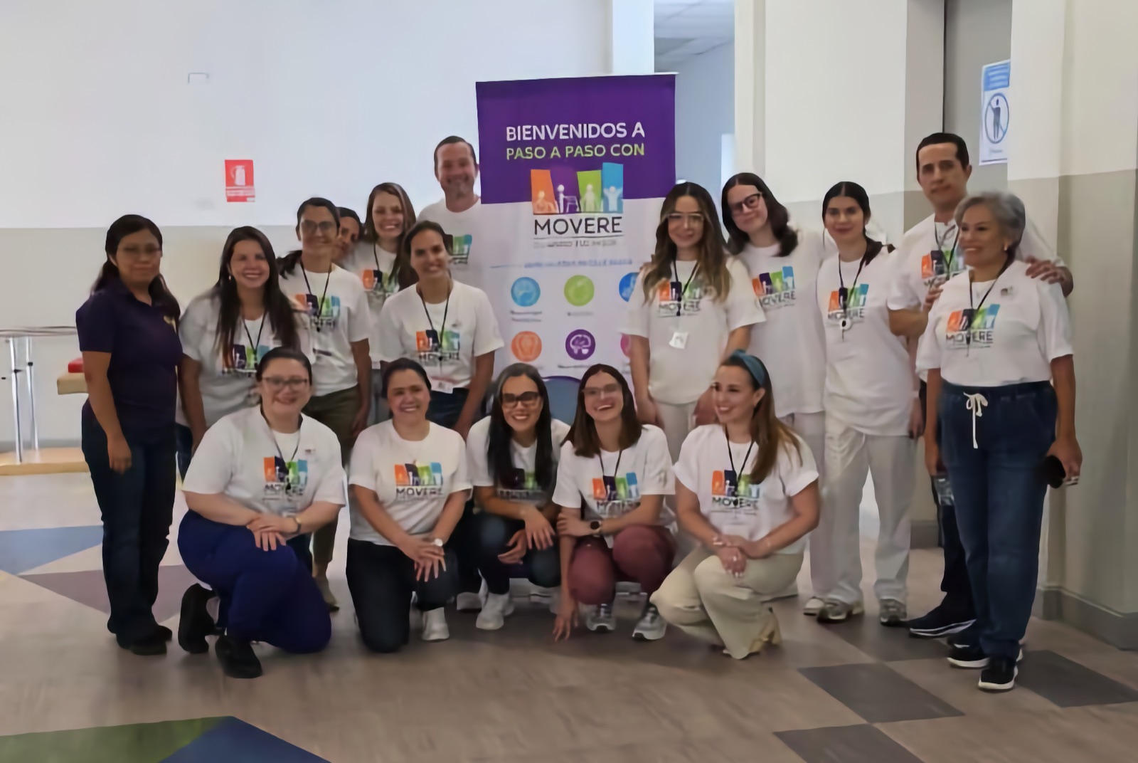 El equipo de especialistas y voluntarios de Fundación Movere, con camisetas blancas del programa, reunido frente al pendón de bienvenida del taller Paso a Paso con Movere